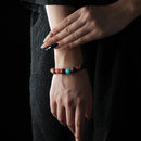Bracelet made of assorted natural crystal beads including lapis lazuli, tiger’s eye, red jasper, aventurine, amethyst, and others, in various vibrant colors, worn on a wrist with a black textured background.