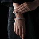 Elegant bracelet featuring a central moonstone, clear quartz beads, and yellow-orange moonstone beads, worn on the wrist against a black lace dress background.