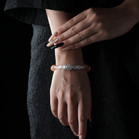Elegant bracelet featuring a central moonstone, clear quartz beads, and yellow-orange moonstone beads, worn on the wrist against a black lace dress background.