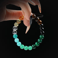 Bracelet composed of various gemstone beads in green, black, yellow, and brown shades, held by hand against a black background.