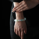 A bracelet featuring faceted natural raw crystals in soft green and pink tones, worn on a wrist against a black textured dress background.