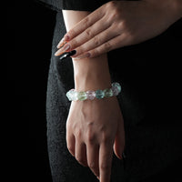 A bracelet featuring faceted natural raw crystals in soft green and pink tones, worn on a wrist against a black textured dress background.