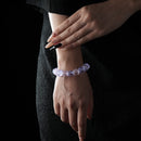 A bracelet made of faceted natural raw crystals in shades of purple and blue, worn on a wrist with a black textured outfit background.