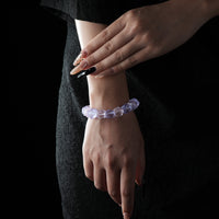 A bracelet made of faceted natural raw crystals in shades of purple and blue, worn on a wrist with a black textured outfit background.