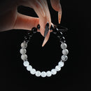 Obsidian, howlite, and white cat eye beaded bracelet with silver accents, held by hand on black background for protection and mental clarity.