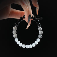 Obsidian, howlite, and white cat eye beaded bracelet with silver accents, held by hand on black background for protection and mental clarity.