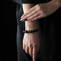 A beaded bracelet featuring black obsidian, tiger's eye, and white crystal beads worn on a woman's wrist, with a dark textured background.