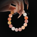 Sunstone and fire quartz beaded bracelet in warm orange and red tones, held by hand on black background for vitality and inner fire.