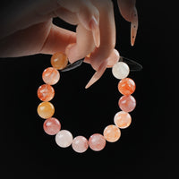 Sunstone and fire quartz beaded bracelet in warm orange and red tones, held by hand on black background for vitality and inner fire.