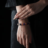 A stylish bracelet featuring alternating purple and orange gemstone beads with a silver butterfly charm, worn on a woman's wrist against a dark background.