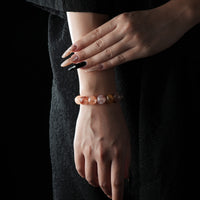 Bracelet made of polished red rutilated quartz beads, featuring vibrant reddish inclusions, worn on a wrist against a dark lace background.