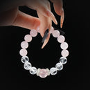 Rose quartz and clear crystal beaded bracelet with silver spacers, held by hand on black background.