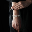Elegant bracelet made of smooth, round snow phantom quartz beads, displayed on a wrist with a dark textured dress background.