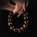 Tiger's eye beaded bracelet with golden-brown chatoyancy, held by hand on black background for confidence and protection.