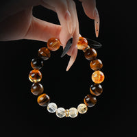 Tiger's eye, citrine, and clear quartz beaded bracelet held by hand on black background for confidence and abundance.