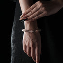 Delicate bracelet featuring white phantom quartz and strawberry quartz beads, worn on wrist with a dark fabric background.